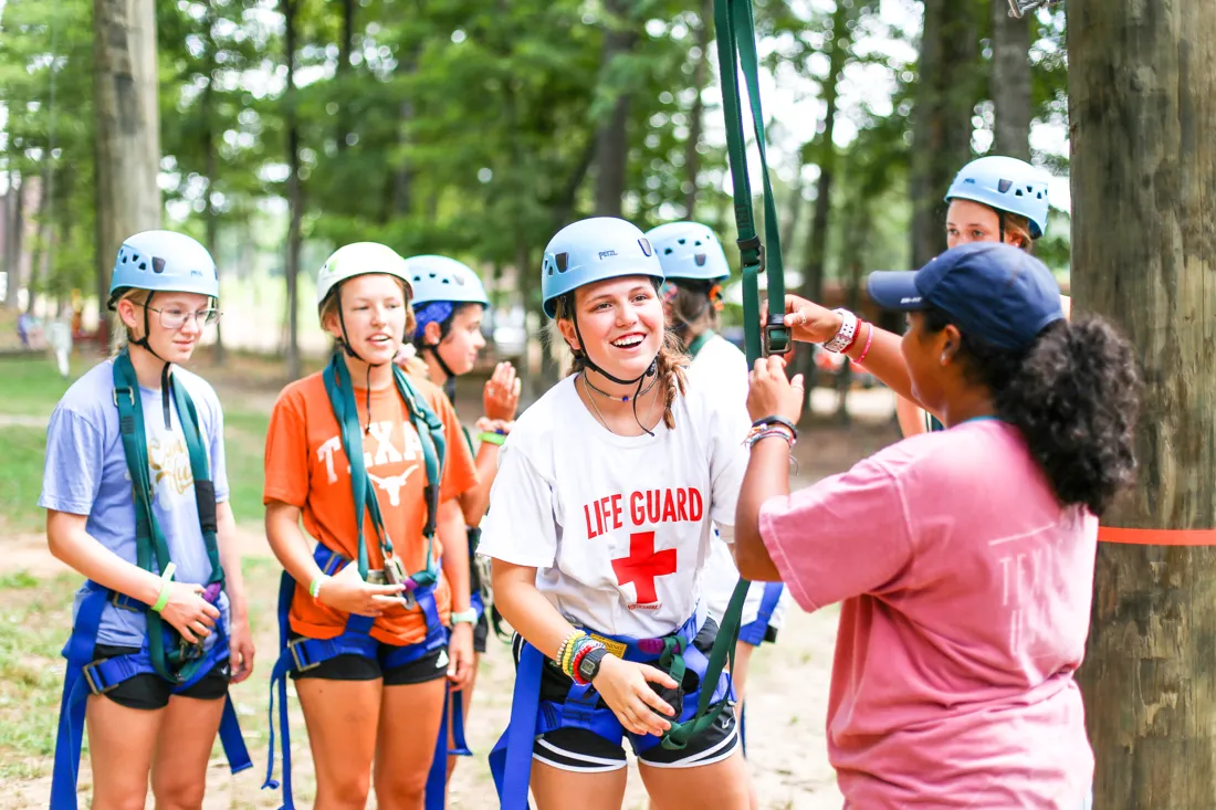 A counselor double-checks a camper's harness rigging before the high ropes course