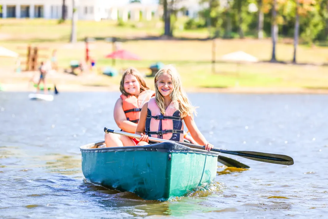 Two campers in properly fitted lifejackets paddling a canoe on Huawni Pond