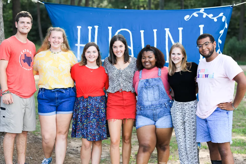 Campers and counselors arm in arm in front of a hand-painted Huawni banner